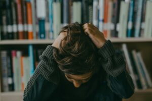 A child appears stressed and frustrated while seated in a library, holding their head.
