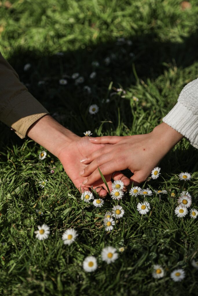 Close-up of romantic hands gently touching on daisies in a grassy field, expressing love and connection.
